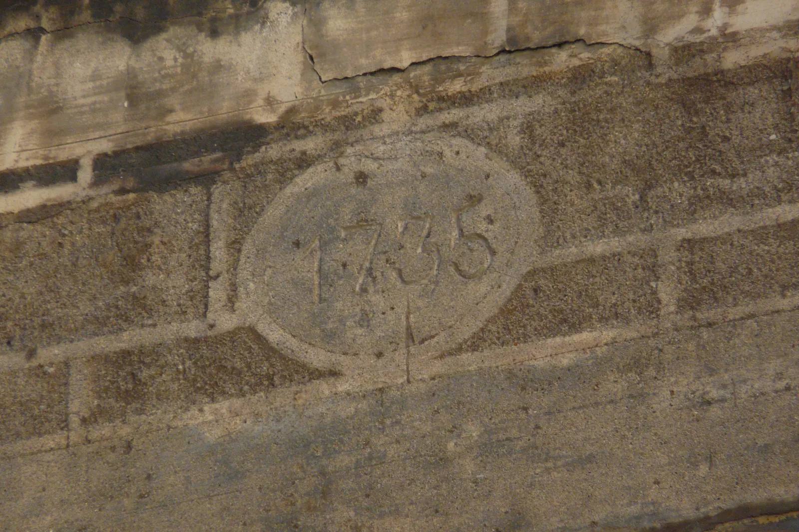 A weathered stone panel carved with the date 1735 inside an oval, set in a wall on Carrer dels Abaixadors
